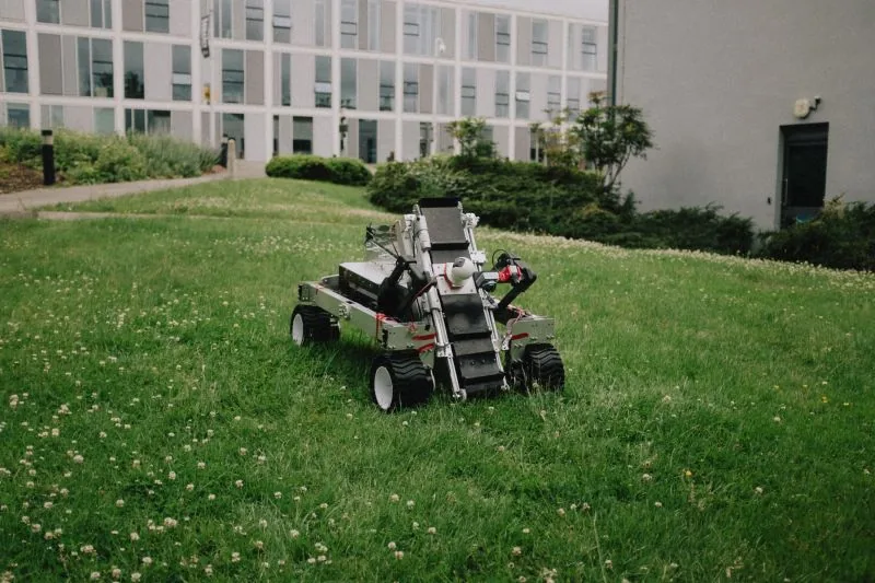 Project MarsWorks rover with its excavator arm, on grass outside the competition building