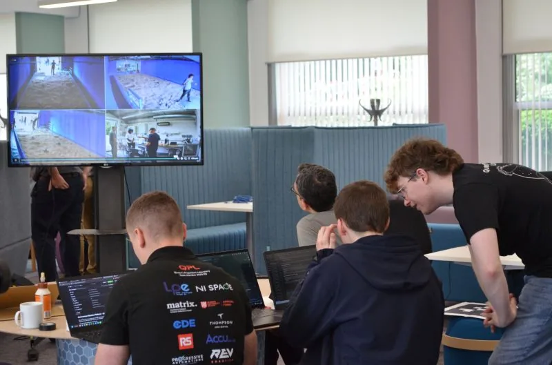 Students at laptops in Mission Control, with arena camera feeds on a large screen