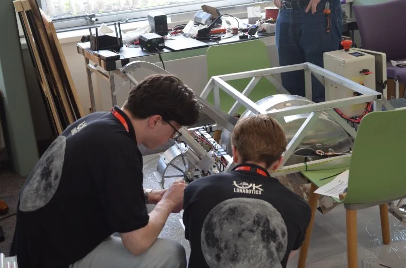 Two students in UK Lunabotics shirts wiring a rover